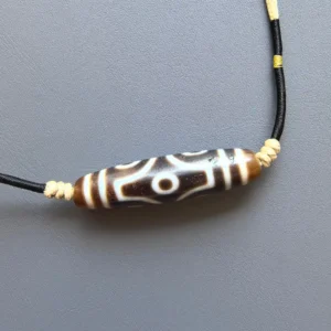Six-eye Dzi bead with white eye and vajra-cross pattern on a black braided cord with cream knotted spacers — Glint & Grain