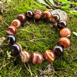 Silk Agate bracelet flatlay on natural grass showing earth-tone banding and grounding energy by Kris Nature