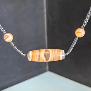 Close-up of natural banded agate barrel bead with crystal eye, Alxa agate accent beads, and hand-braided black cord detail