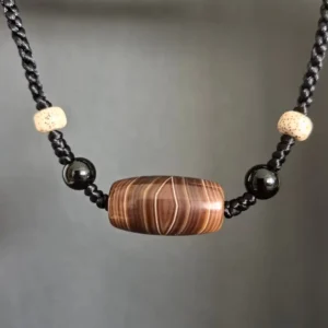 Front close-up of Vajra Eye Silk Agate barrel pendant with natural black agate beads, Star Moon Bodhi seed accents, and hand-braided cord