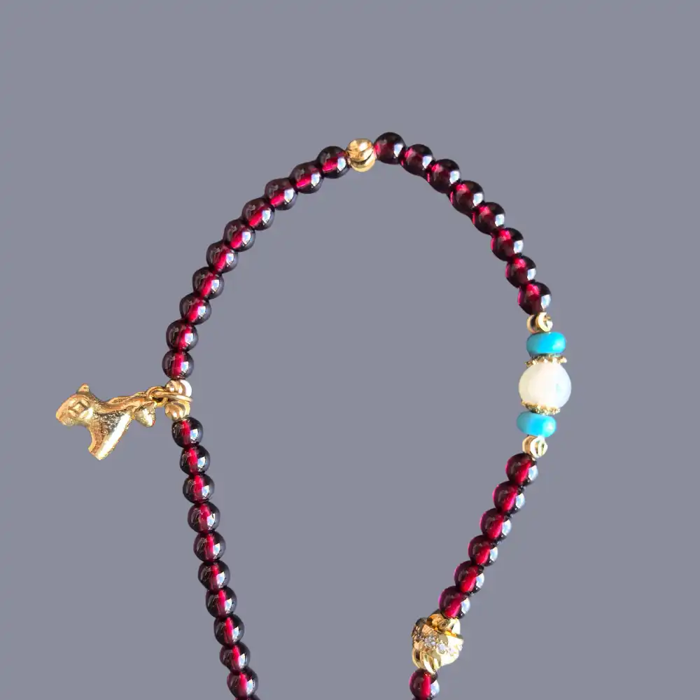 Close view of natural garnet beads, copper-gold horse charm, and peace-abundance medallion on a 3-wrap bracelet | Glint & Grain
