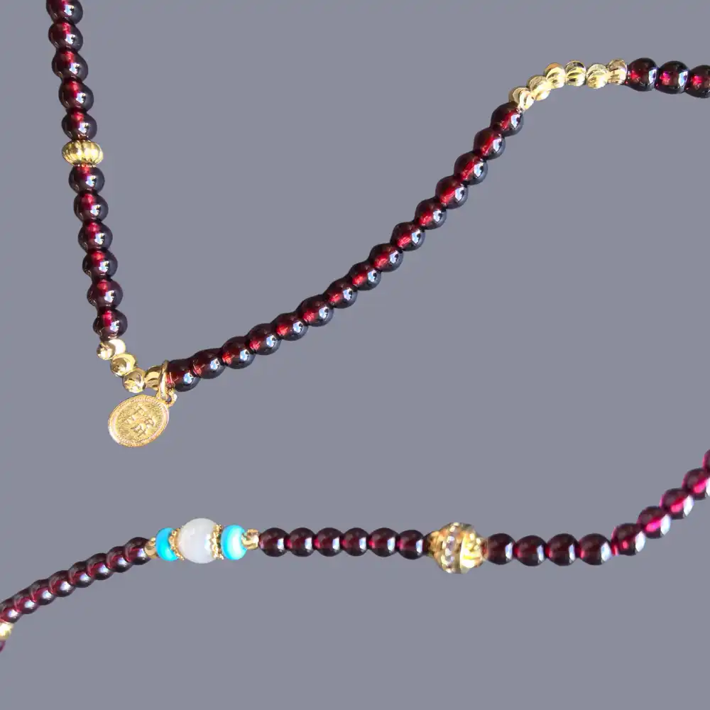Detail of gold-tone charms and faceted garnet beads on a 3-wrap bracelet | Glint & Grain
