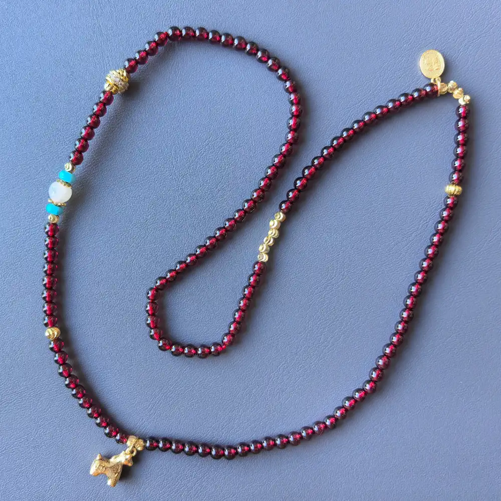 Garnet 3-wrap bracelet flat-lay on leather with horse charm and medallion | Glint & Grain