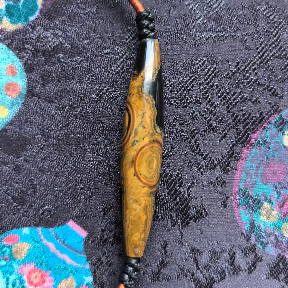 Front detail of two-eye Mongolian eye-stone lance pendant with hand-braided black cord and copper thread wrap | Glint & Grain