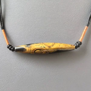 Material detail of the two-eye eye-stone lance pendant, showing weathered ochre-black texture and copper-toned thread wrap | Glint & Grain