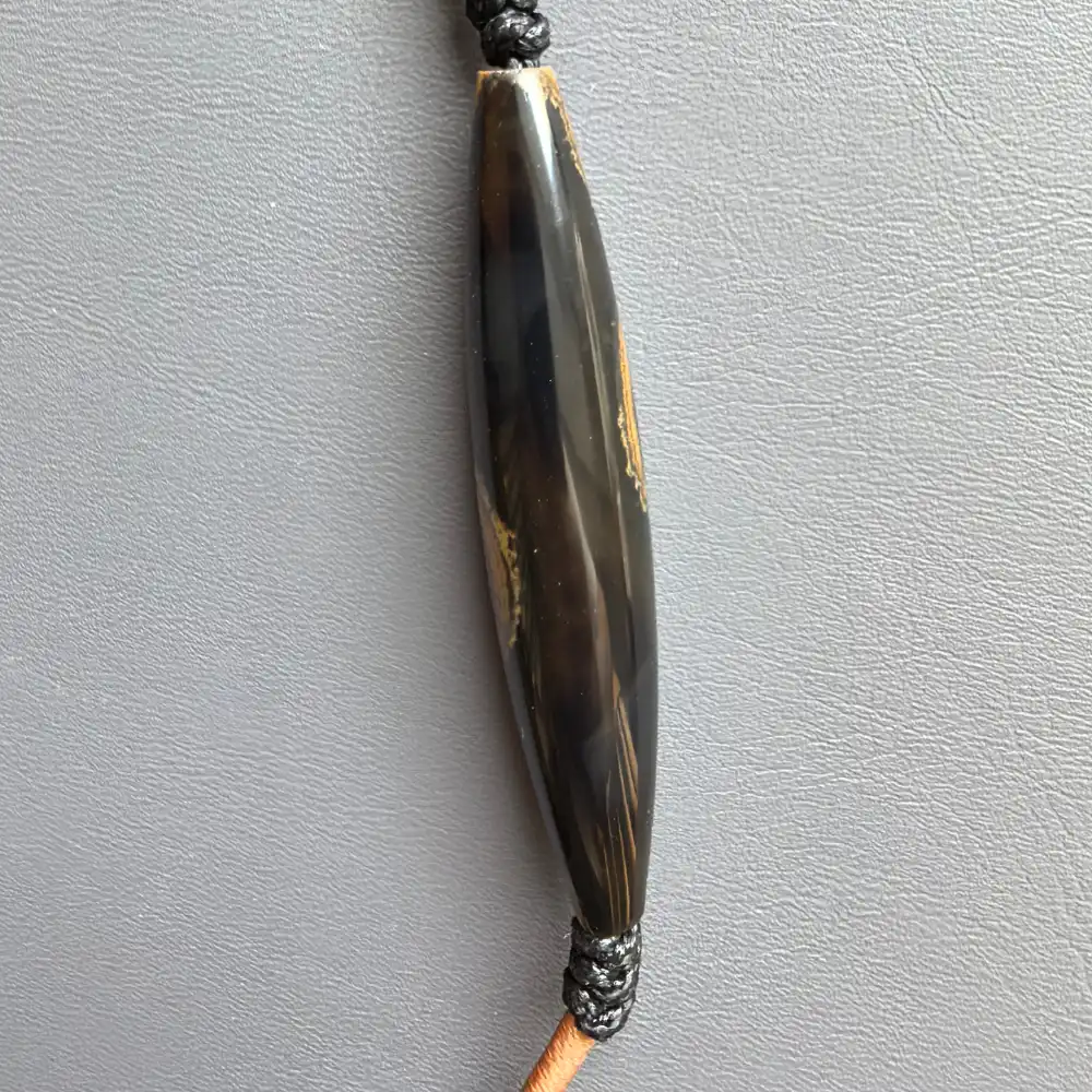 Side view of the two-eye eye-stone lance pendant showing glossy black amber-toned surface | Glint & Grain