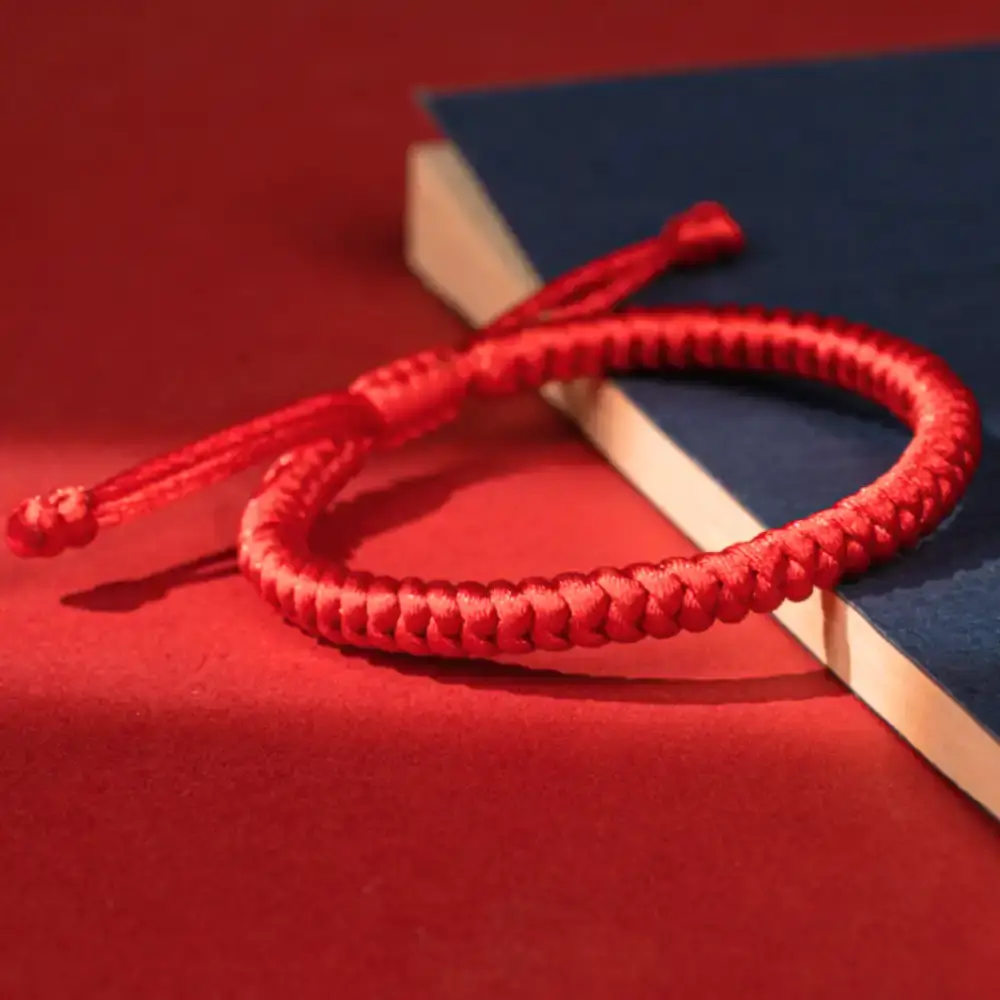 Red string bracelet on a blue notebook, Tibetan Vajra knot handmade nylon cord