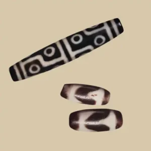lTwo Dzi beads on a beige background — a long multi-eye bead with dark line motifs, above a tiger-tooth Dzi shown from the front and the back.