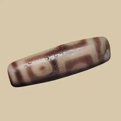 Close view of a polished Dzi bead's surface showing weathering texture — fine crazing lines and small pit marks across the cream and dark brown eye pattern.