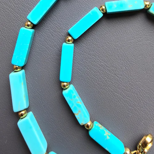 Close-up of the magnesite turquoise tube beads and small gold-tone spacer beads on a charcoal background.
