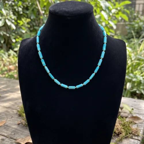 Magnesite turquoise necklace displayed on a black neck bust against a soft green outdoor background.