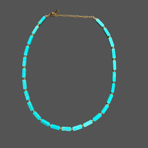 Magnesite turquoise necklace laid in a long oval, with gold-tone spacers and the extender chain visible.